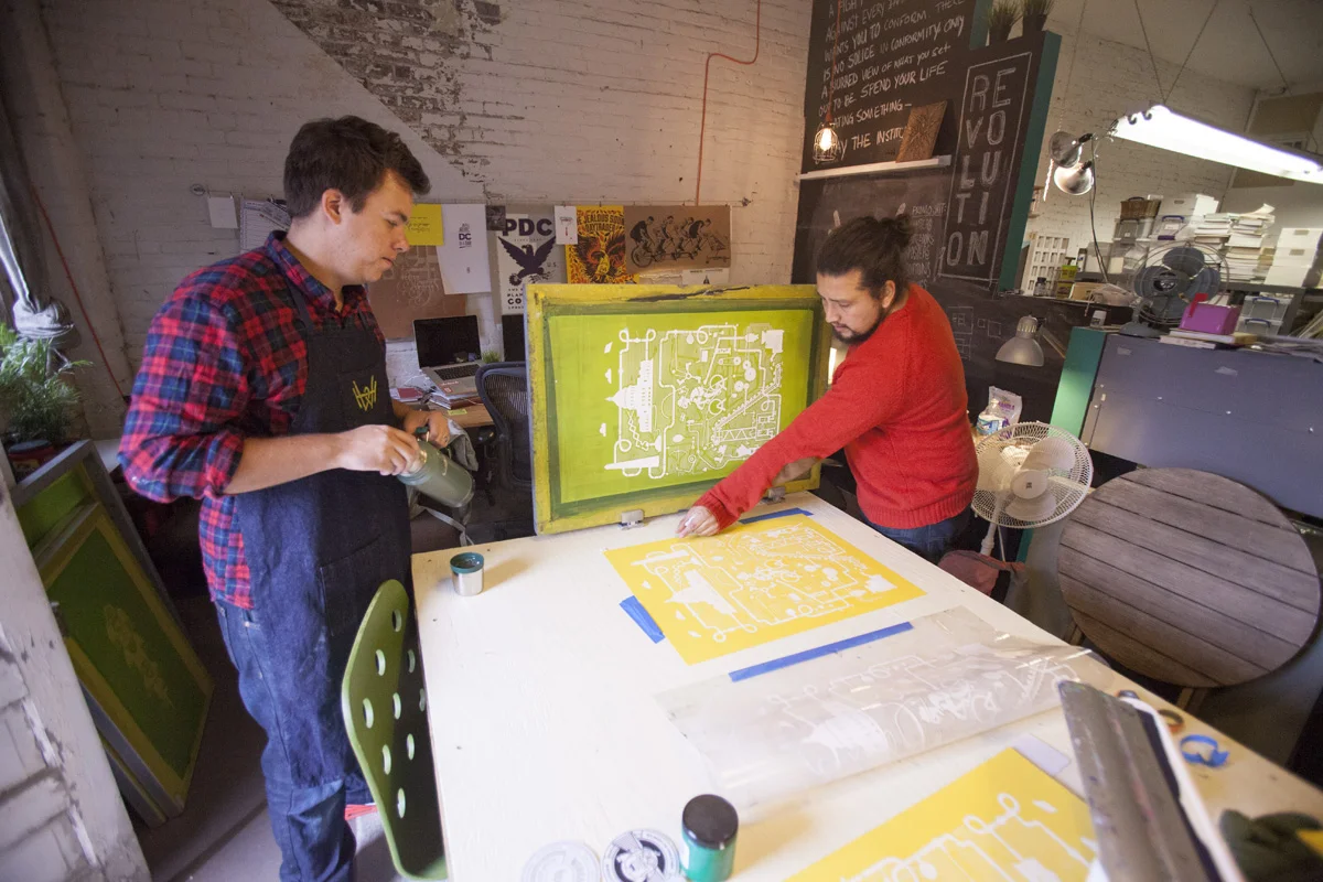 Two of the studio team registering a yellow Artcrank poster against a green emulsion screen.