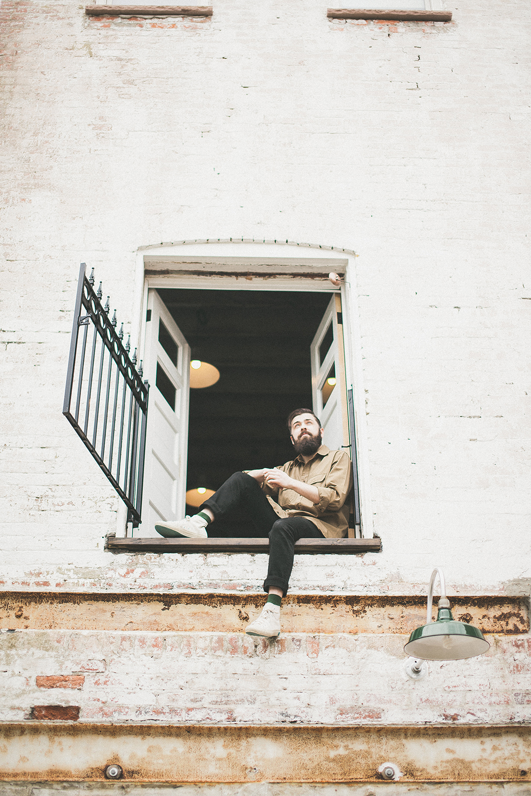 Greg sitting in the second-floor window of the carriage house, against painted brick.